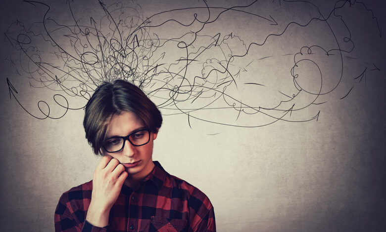 Closeup portrait of sad and thoughtful teen guy, hand under cheek, looking down feel headache, isolated on grey wall. Upset boy experiencing adolescence crisis as mess lines coming out of head.